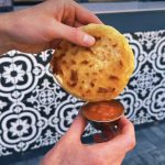 A Pupusa dipping in salsa roja for an explosion of flavors in your month.